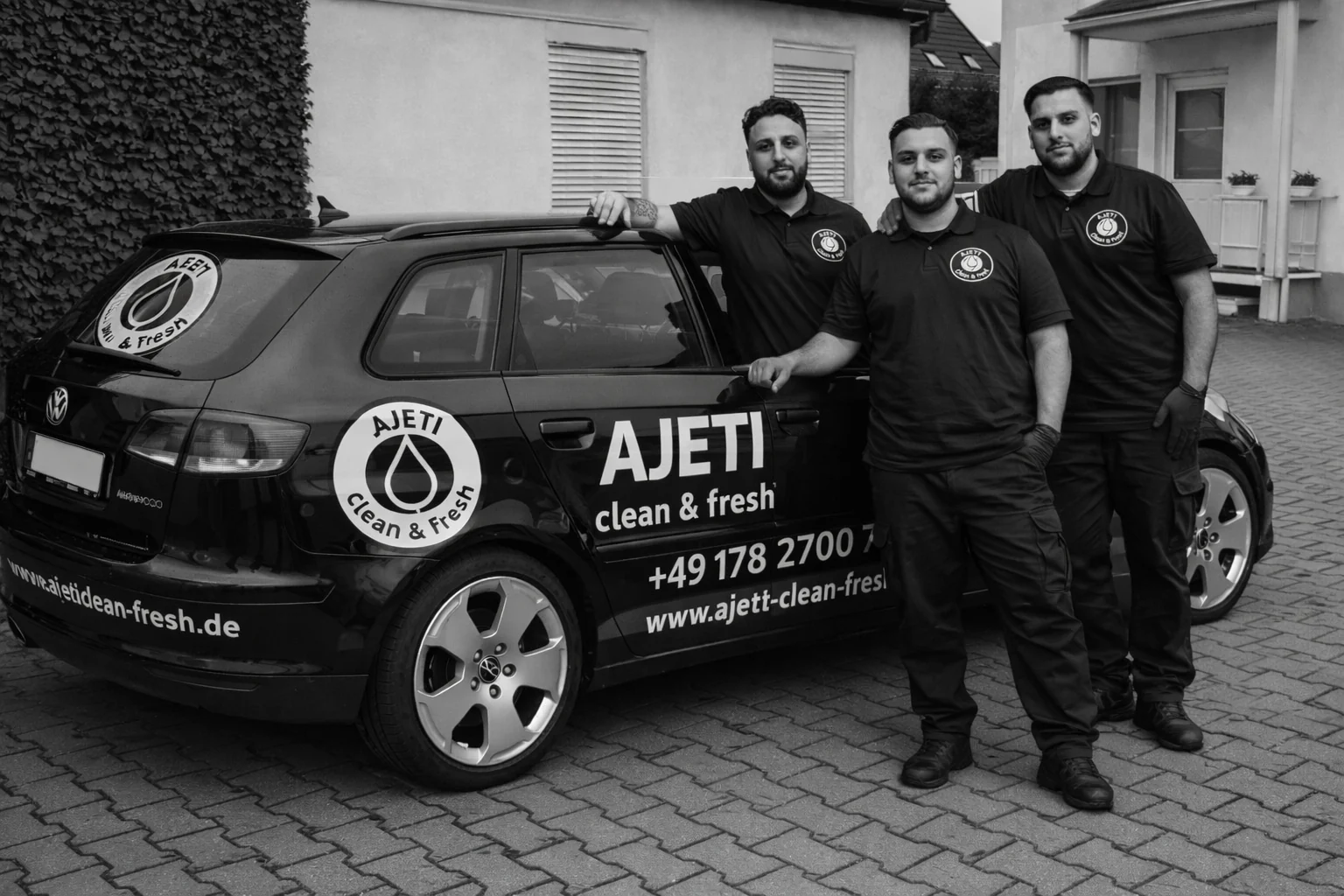 Drei Mitarbeiter von AJETI clean & fresh vor dem beschrifteten Firmenfahrzeug, Schwarz-Weiß-Aufnahme